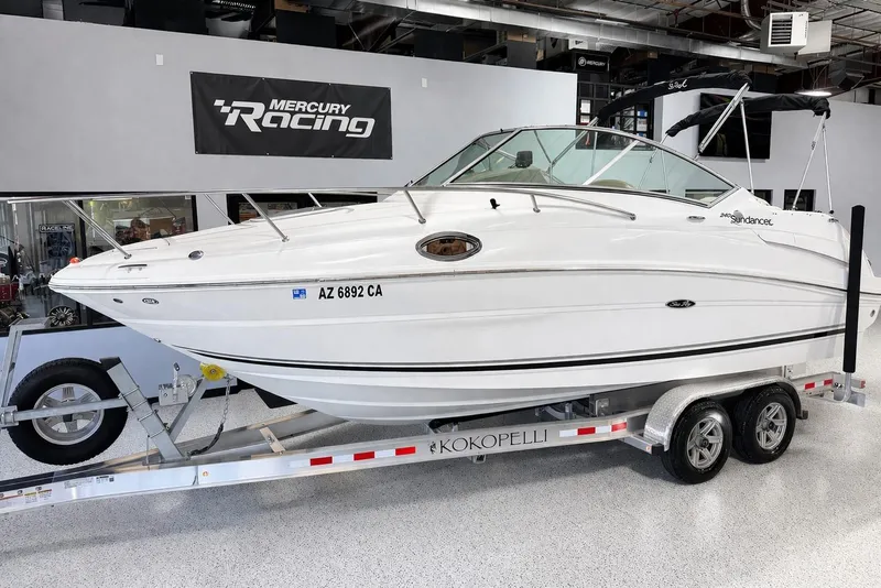 The Image of 2009 Sea Ray 240 Sundancer boat on trailer in showroom, Mercury Racing sign above. - 0