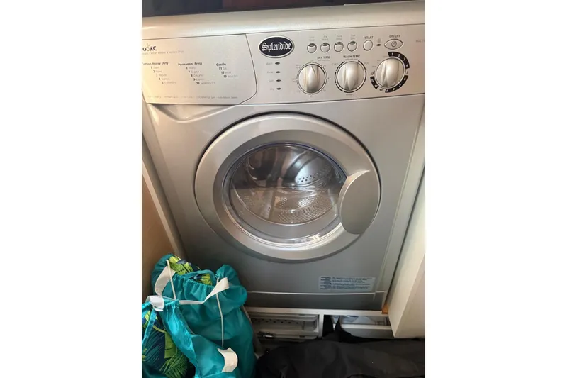 Slide: The Image of Splendide washing machine inside a 2018 Jeanneau 51 yacht, with laundry bag nearby. - 30