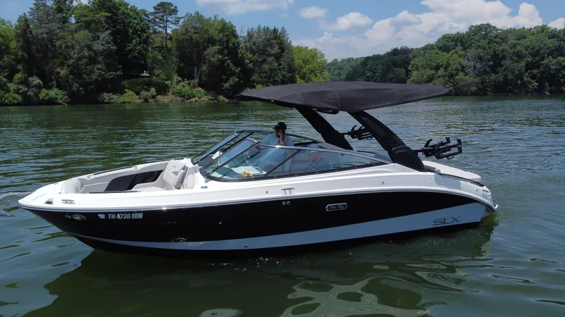 The Image of 2023 Sea Ray SLX 260 Surf boat on a serene lake with lush greenery. - 0
