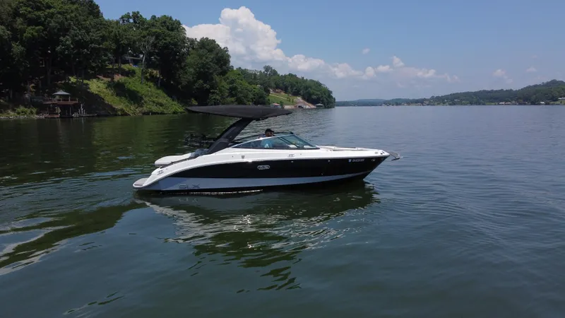 Slide: The Image of 2023 Sea Ray SLX 260 Surf boat cruising on a serene lake with lush green shoreline. - 1