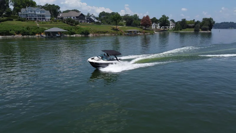 Slide: The Image of 2023 Sea Ray SLX 260 Surf boat cruising on a scenic lake with waterfront homes. - 12