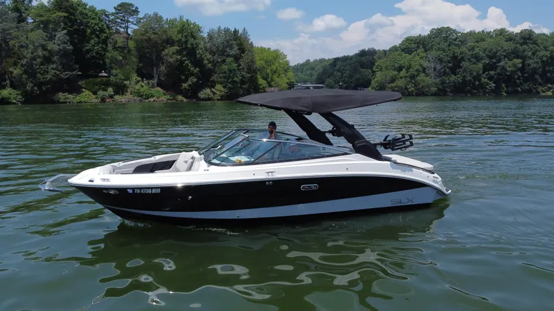 Slide: The Image of 2023 Sea Ray SLX 260 Surf boat on a serene lake with lush green surroundings. - 14