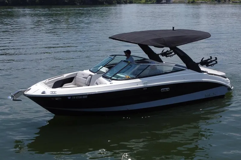 Slide: The Image of 2023 Sea Ray SLX 260 Surf boat on calm lake with lush green shoreline. - 2