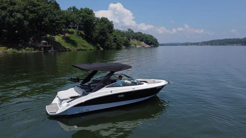 Slide: The Image of 2023 Sea Ray SLX 260 Surf boat cruising on a serene lake with lush green shoreline. - 7