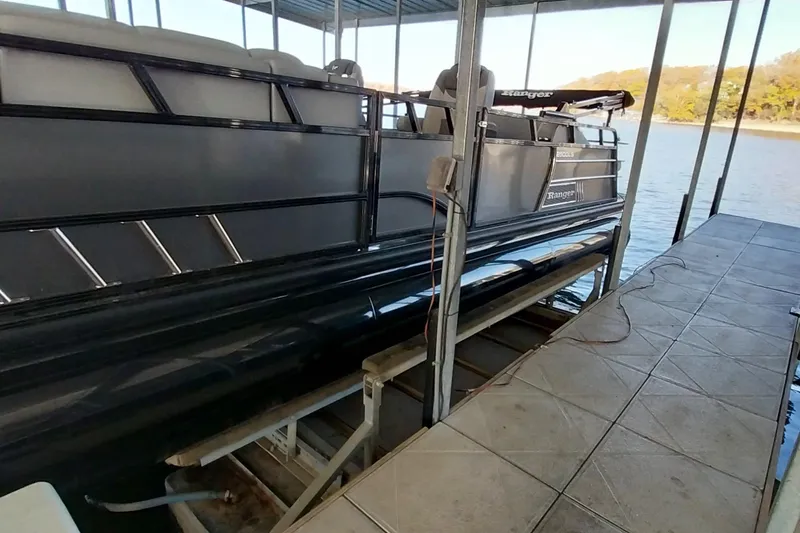 Slide: The Image of 2023 Ranger 2500LS pontoon boat docked on a lake under a covered structure. - 52