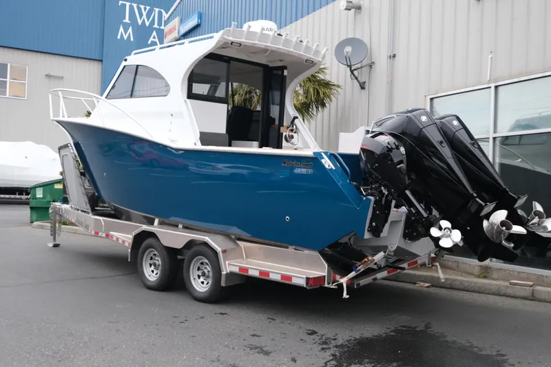 Slide: The Image of 2026 Makaira 28 boat on trailer, blue hull, twin outboard motors, parked outside a building. - 4