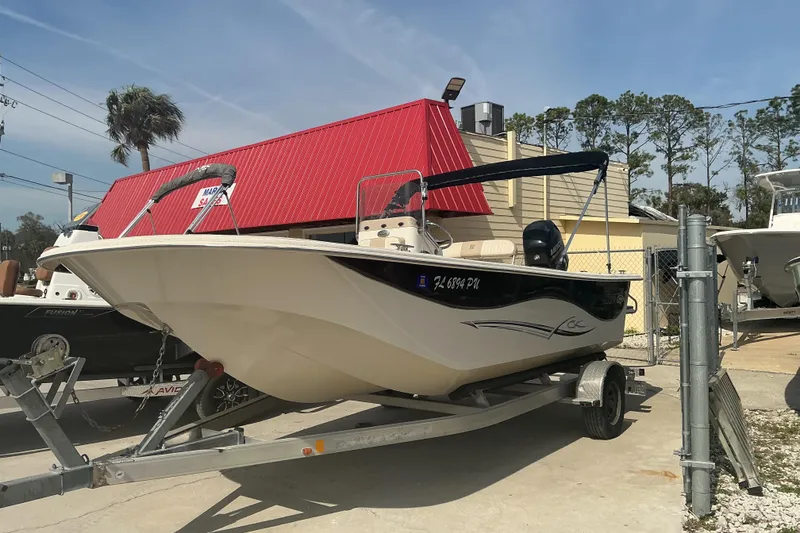 Slide: The Image of 2014 Carolina Skiff 198 DLV boat on trailer, parked outdoors near a red-roofed building. - 14