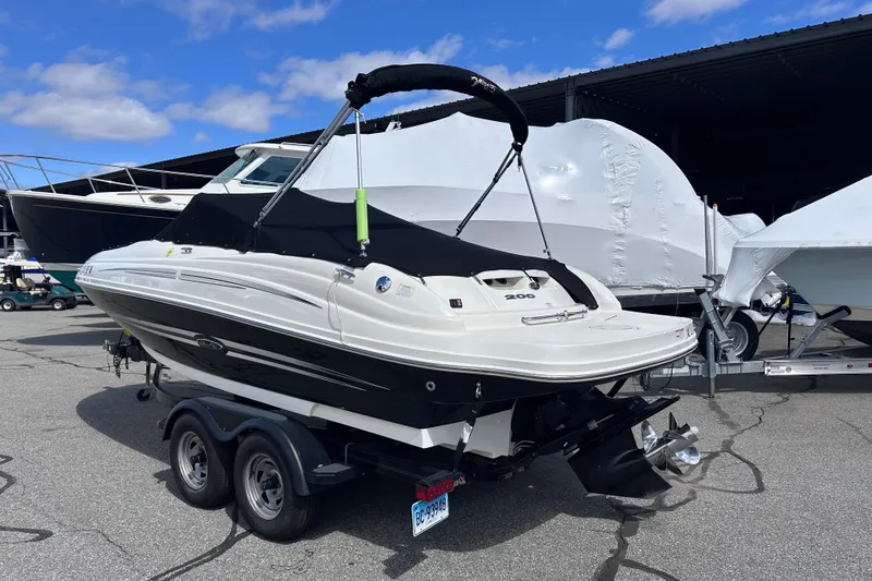 Slide: The Image of 2012 Sea Ray 200 Sundeck boat on trailer, parked outdoors under blue sky. - 3
