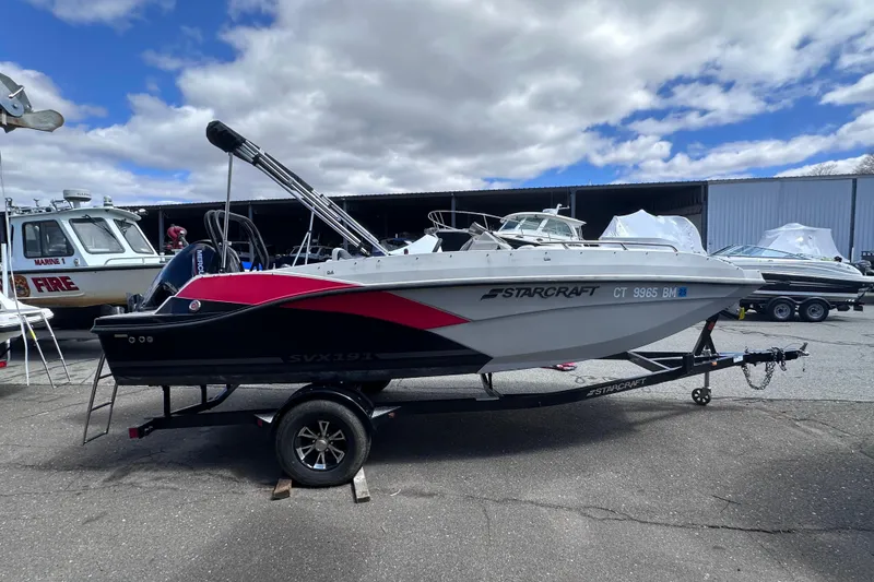 Slide: The Image of 2023 Starcraft SVX 191 OB boat on trailer, parked outdoors under cloudy sky. - 2