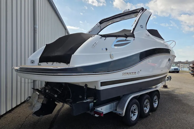The Image of 2014 Rinker 290 Express Cruiser on trailer, parked beside a building. - 0