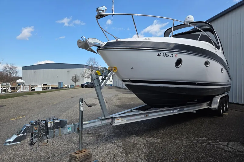 Slide: The Image of 2014 Rinker 290 Express Cruiser on trailer, parked outdoors near a warehouse. - 2