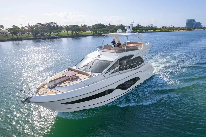 Slide: The Image of 2018 Sunseeker Manhattan 52 yacht cruising on a sunny day, surrounded by lush greenery. - 10