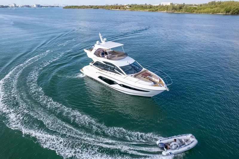 Slide: The Image of 2018 Sunseeker Manhattan 52 yacht cruising with a small boat on open water. - 12