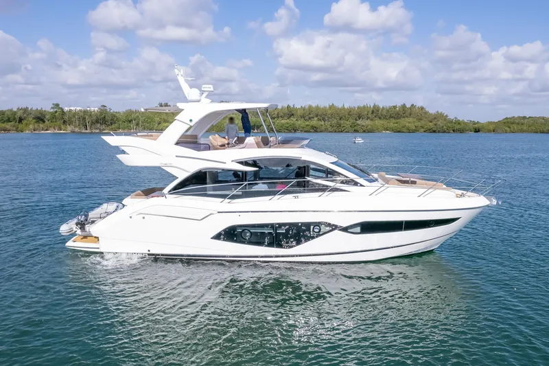 Slide: The Image of 2018 Sunseeker Manhattan 52 yacht cruising on a serene blue lake under a partly cloudy sky. - 2