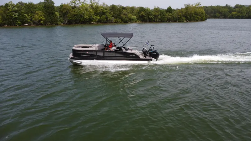 Slide: The Image of 2023 Barletta Corsa 23UC pontoon boat cruising on a lake with lush green shoreline. - 7