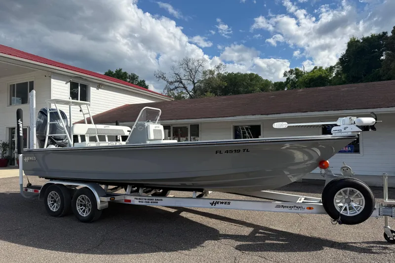 Slide: The Image of 2023 Hewes Redfisher 21 boat on trailer, parked outside a building under a cloudy sky. - 2