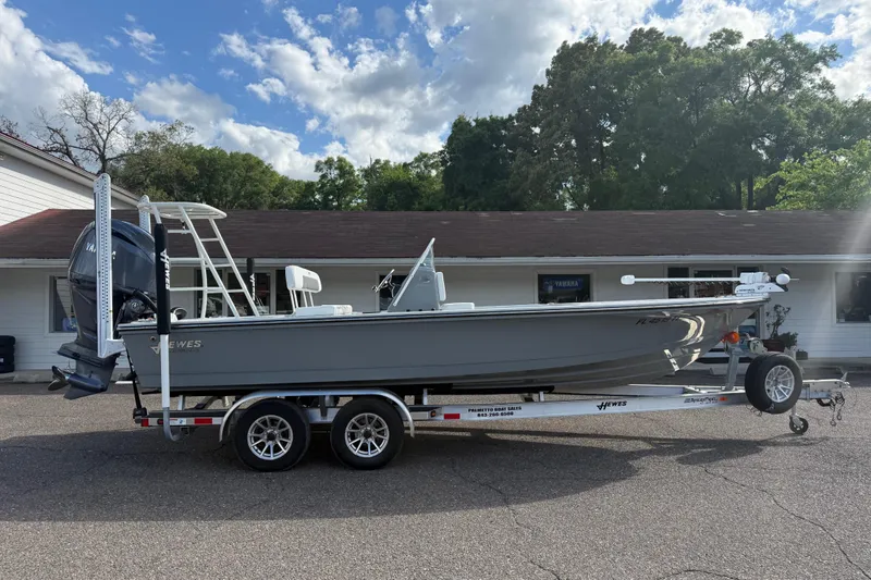 Slide: The Image of 2023 Hewes Redfisher 21 boat on trailer, parked outside a building under a cloudy sky. - 4