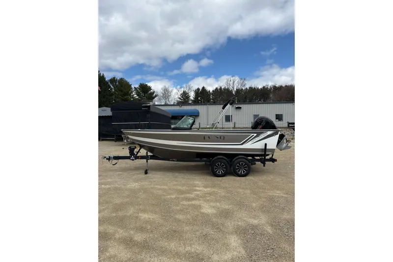The Image of 2026 Lund 1875 Fisherman boat on trailer, parked outdoors under a cloudy sky. - 0