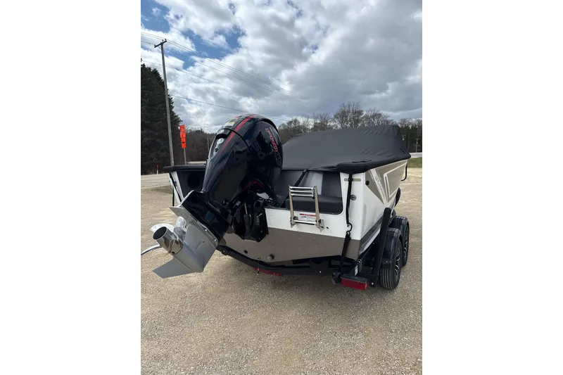 Slide: The Image of 2026 Lund 1875 Fisherman boat with outboard motor, parked on gravel under cloudy sky. - 9