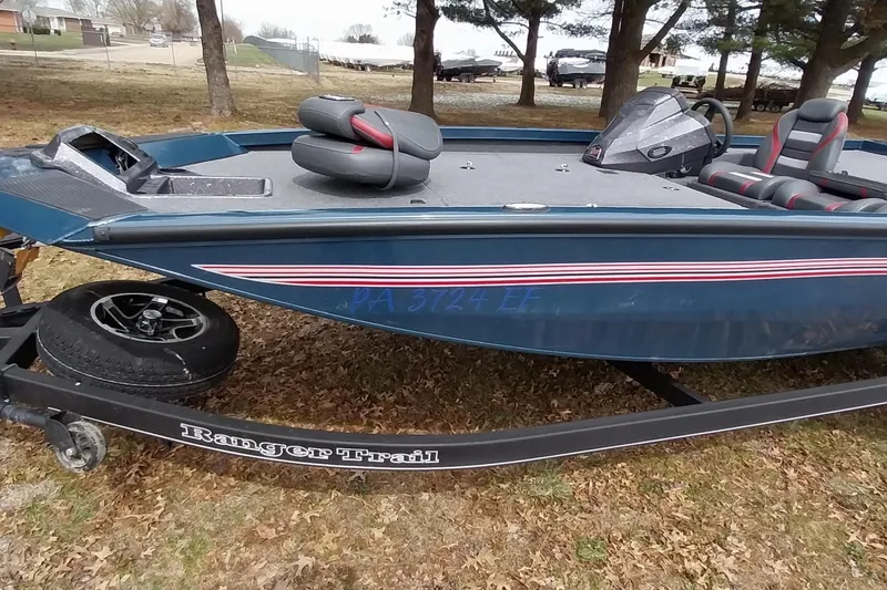 Slide: The Image of 2024 Ranger RT198P boat on trailer, parked on grass with trees in background. - 29