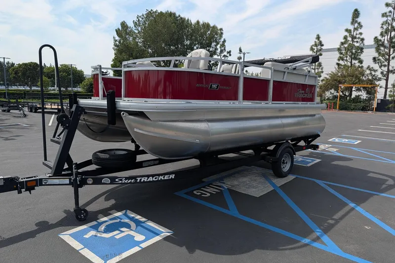 Slide: The Image of 2026 Sun Tracker Bass Buggy 16 XL Select pontoon boat on trailer in parking lot. - 2