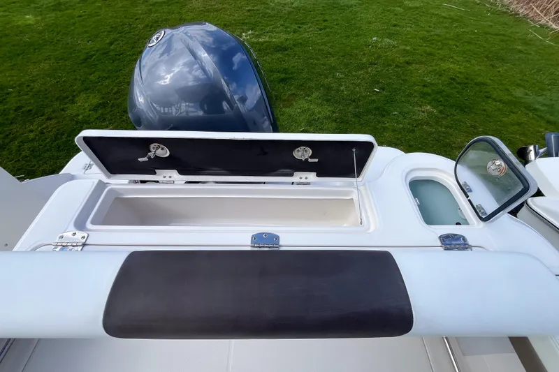 Slide: The Image of 2020 Robalo R247 Dual Console boat with open storage compartment and motor, on grassy background. - 5
