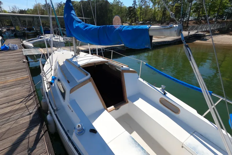 Slide: The Image of 1983 Catalina 25 sailboat docked, featuring blue sail cover and open cabin entrance. - 6