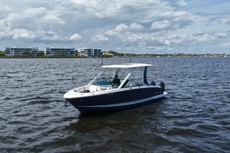 Slide: The Image of 2022 Chaparral 280 OSX boat on a calm lake with modern buildings in the background. - 10
