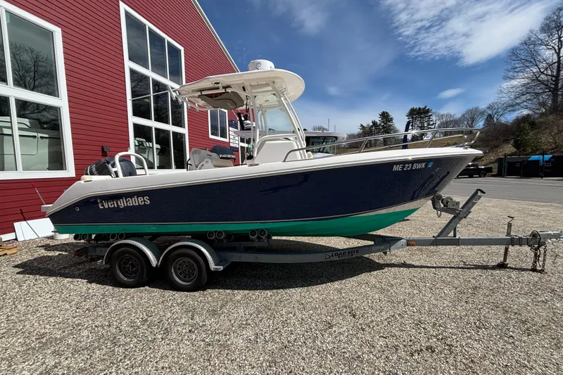 The Image of 2011 Everglades 230 Center Console boat on trailer, parked near red building. - 0