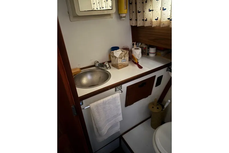 Slide: The Image of 1973 Luhrs 28 boat bathroom with sink, toiletries, and nautical-themed curtains. - 24