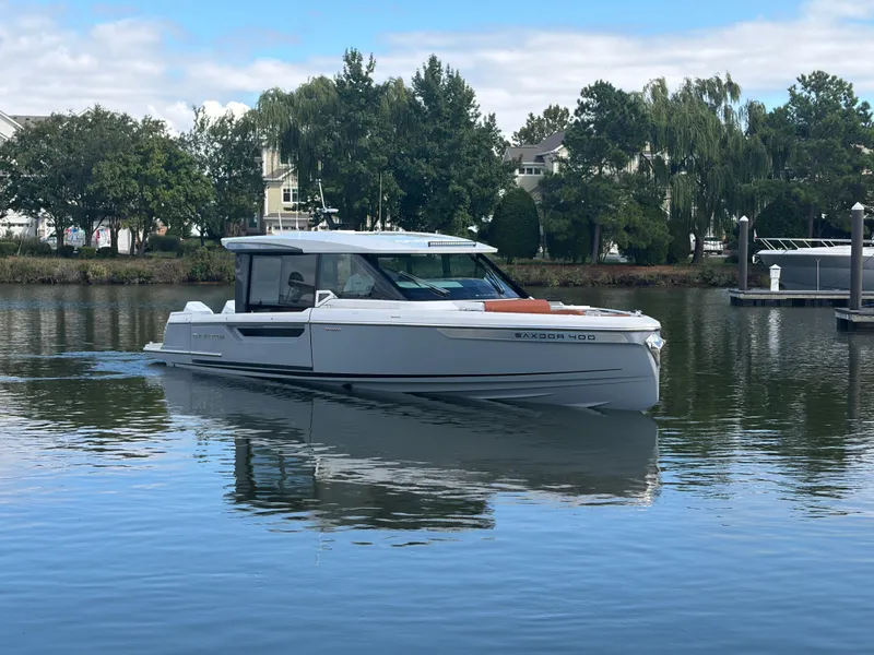 Slide: The Image of A 2027 Saxdor 400 GTC cruising on calm waters, surrounded by trees and buildings. - 1