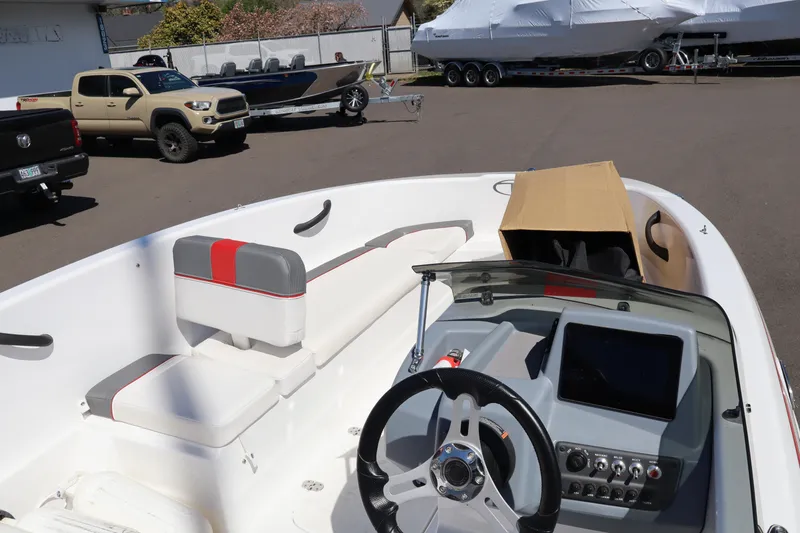 Slide: The Image of 2023 White River Tahoe boat interior with steering wheel and seating, parked near trucks and trailers. - 13