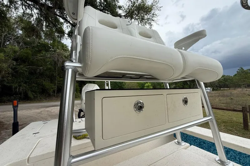 Slide: The Image of 2021 Young Boats Gulf Shores 24 helm seat with storage drawers, set against a natural backdrop. - 12