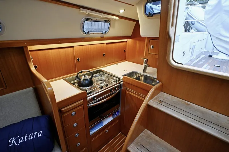 Slide: The Image of Interior of 2020 Hallberg Rassy 310 yacht, featuring a compact kitchen with wooden cabinetry. - 10
