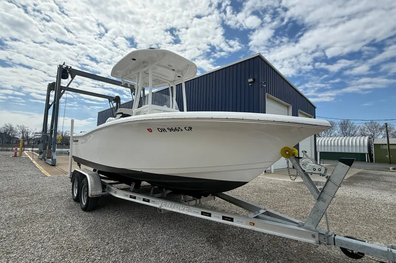 Slide: The Image of 2025 Tidewater 198 CC Adventure boat on trailer, parked near a blue warehouse under a cloudy sky. - 20