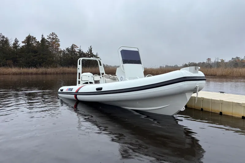 Slide: The Image of 2026 Airrib 18 inflatable boat docked on calm water, surrounded by trees. - 5