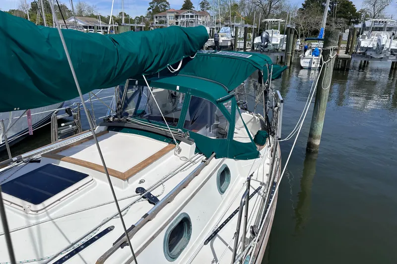 Slide: The Image of 1986 Pacific Seacraft 34 sailboat docked, featuring green canvas covers and a sleek design. - 7