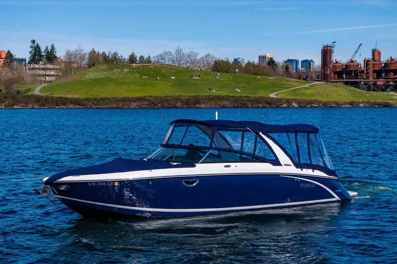 Slide: The Image of 2019 Cobalt R30 boat cruising on a scenic lake with city skyline backdrop. - 2