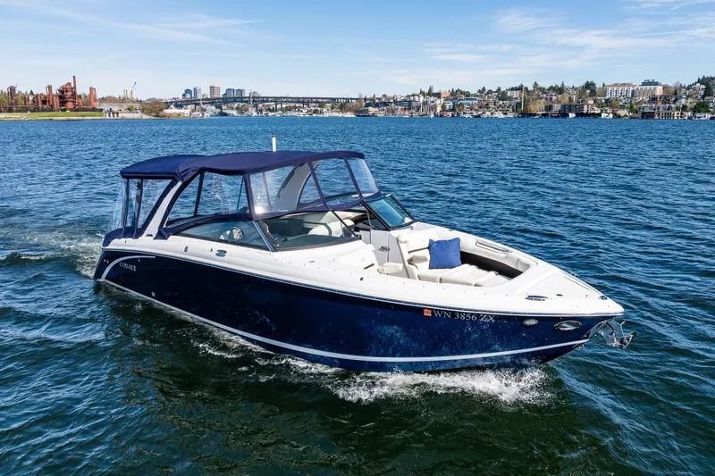 Slide: The Image of 2019 Cobalt R30 boat cruising on a scenic lake with city skyline backdrop. - 26