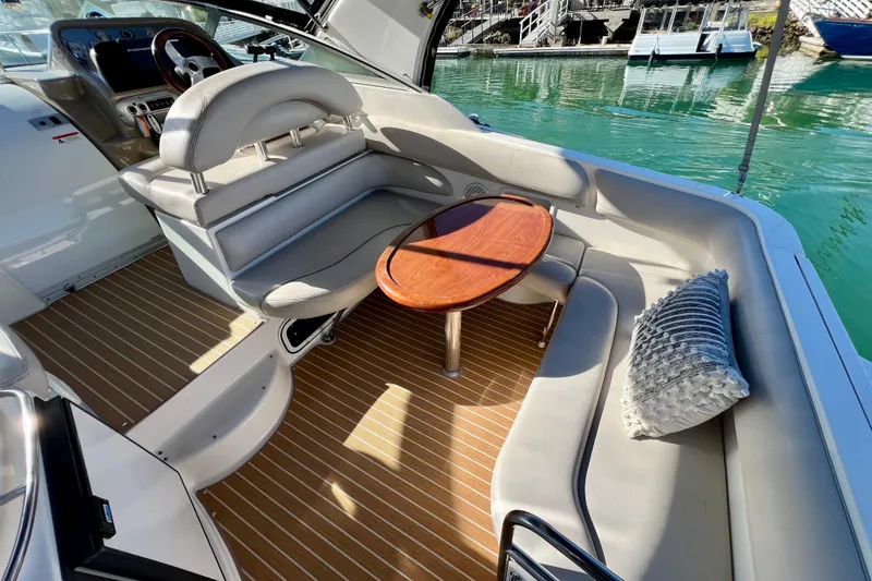 Slide: The Image of 2007 Larson Cabrio 310 boat interior with seating, table, and cushion, docked by the water. - 14