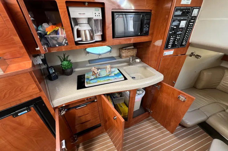 Slide: The Image of 2007 Larson Cabrio 310 boat interior with kitchenette, featuring microwave, coffee maker, and wooden cabinetry. - 37