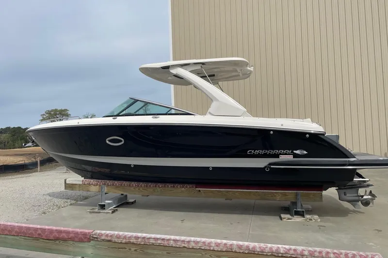 Slide: The Image of 2019 Chaparral 297 SSX boat on display, black hull, white top, outdoor setting. - 14