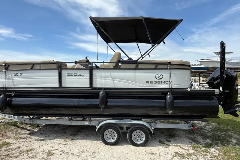 The Image of 2023 Regency 230 DL3 pontoon boat on trailer, featuring a black canopy. - 0