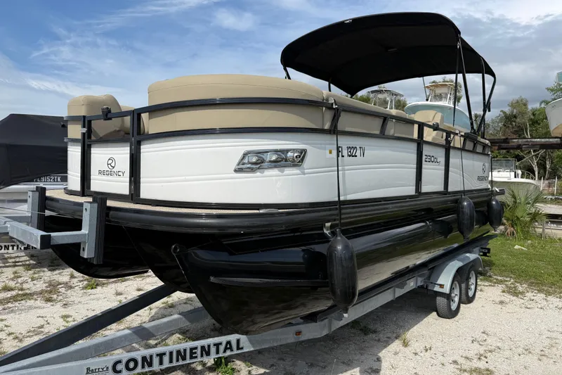 Slide: The Image of 2023 Regency 230 DL3 pontoon boat on a trailer, parked outdoors. - 2