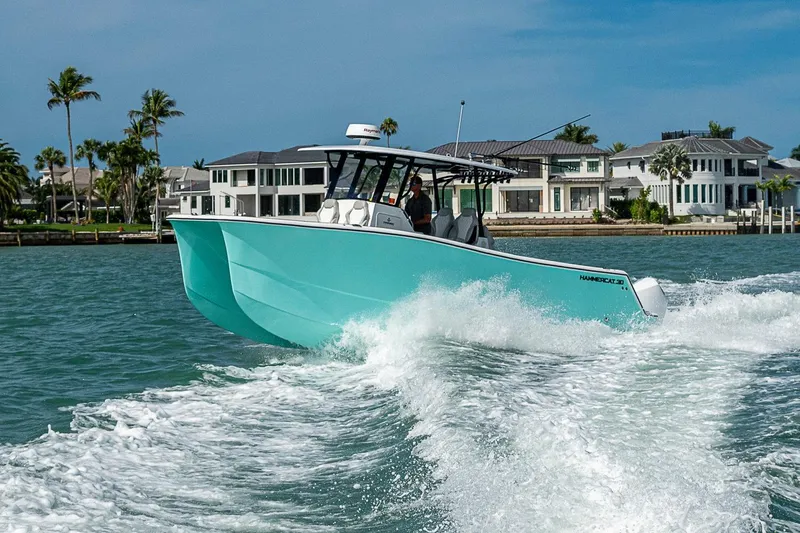 Slide: The Image of 2025 Hammer Yachts 30 cruising on turquoise waters near luxury waterfront homes. - 14