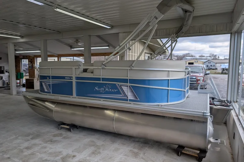 Slide: The Image of 2026 SunChaser Vista 16 LR pontoon boat displayed indoors, featuring sleek blue design. - 5