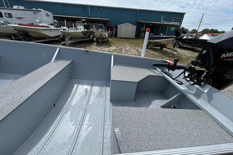 Slide: The Image of 2026 Crestliner 1672 Outreach boat interior with motor, parked outdoors near other boats. - 12