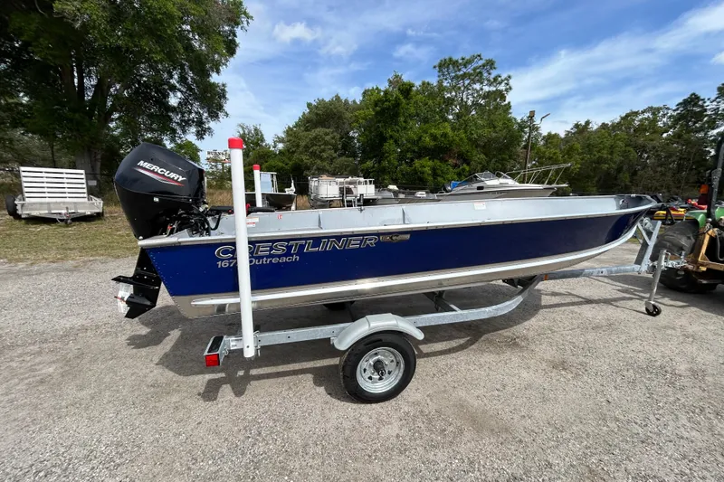 Slide: The Image of 2026 Crestliner 1672 Outreach boat on trailer, parked outdoors with trees in background. - 4