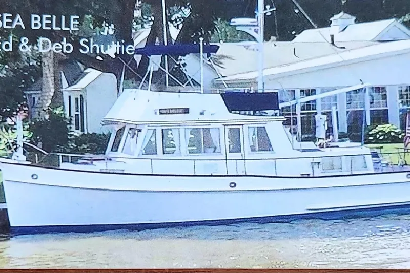 Slide: The Image of 1987 Grand Banks 36 Classic yacht docked by a house, featuring a white hull and blue canopy. - 3