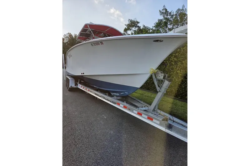 Slide: The Image of 2002 Ocean Runner 30 boat on trailer, parked on a road with trees in background. - 2